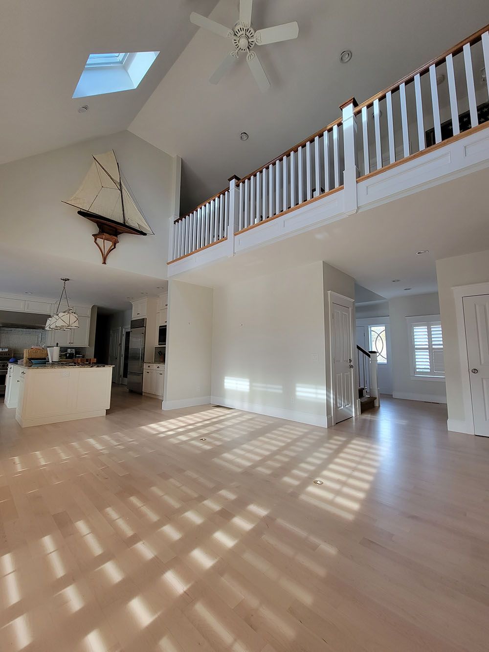 Bright, empty living room with high ceilings, skylights, and sunlit floors.