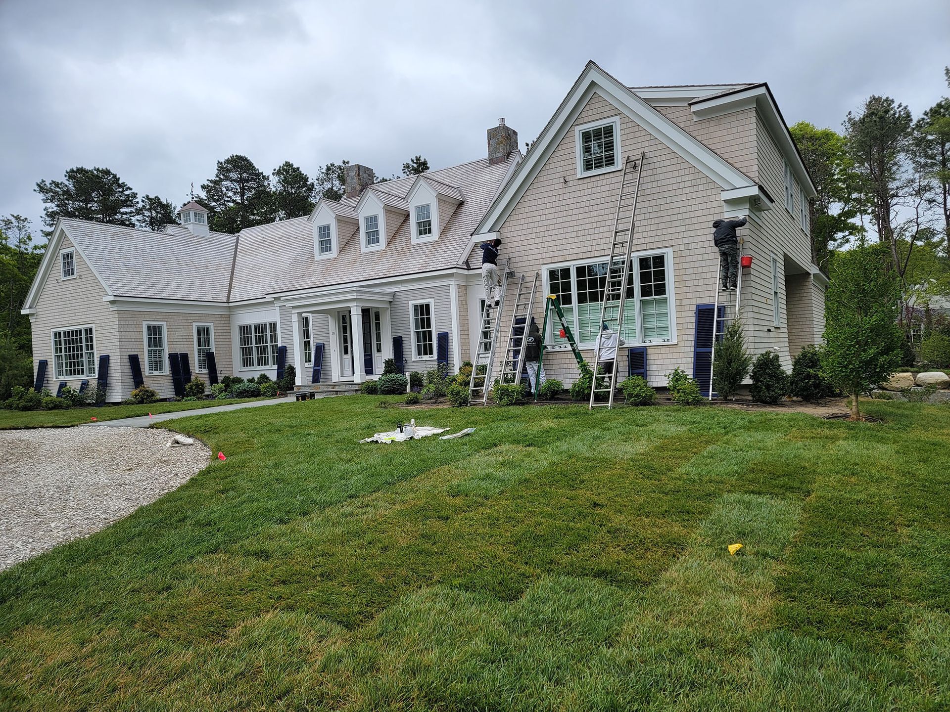 Large gray house with white trim and a green lawn on an overcast day