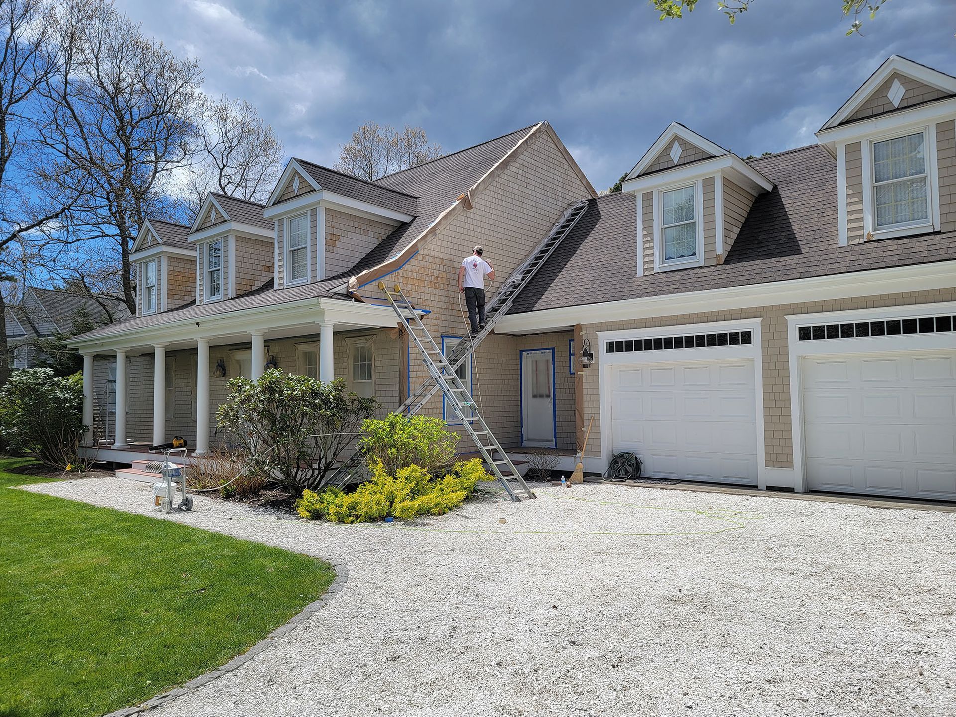 Suburban house with two garage doors, covered porch, and gravel driveway under a blue sky