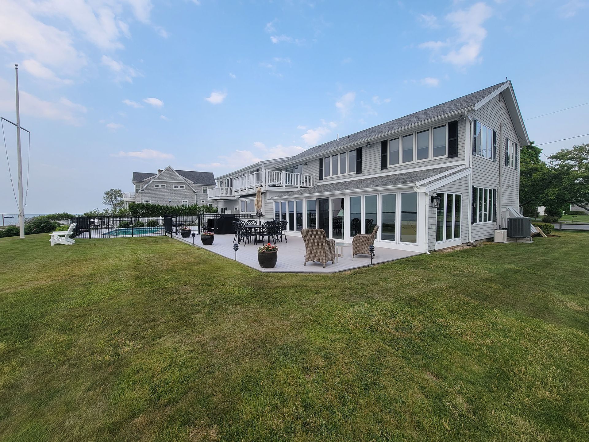 White seaside house with large windows, patio seating, and green lawn under a blue sky