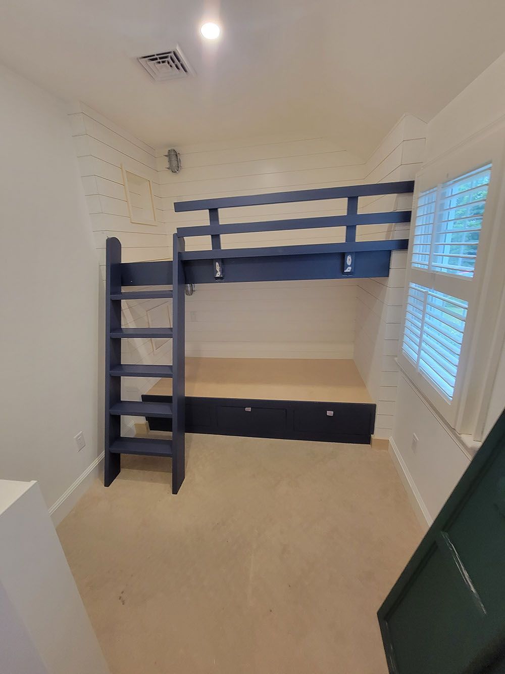 Small bedroom with dark blue bunk bed, white walls, beige carpet, and a window with blinds.