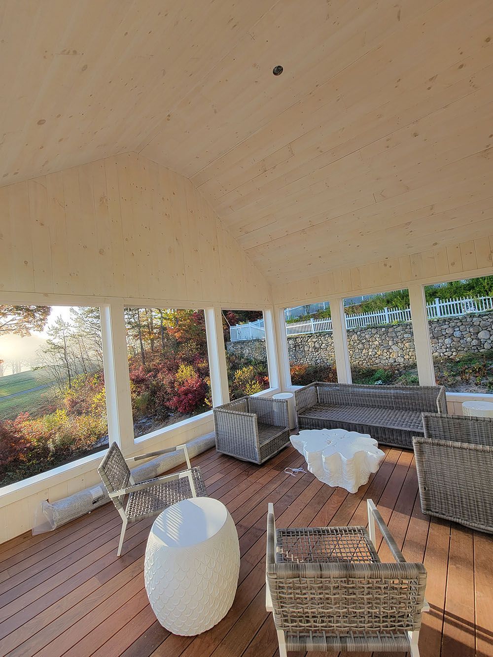 Covered patio with wicker seating, a white table, and an ottoman overlooking a garden.