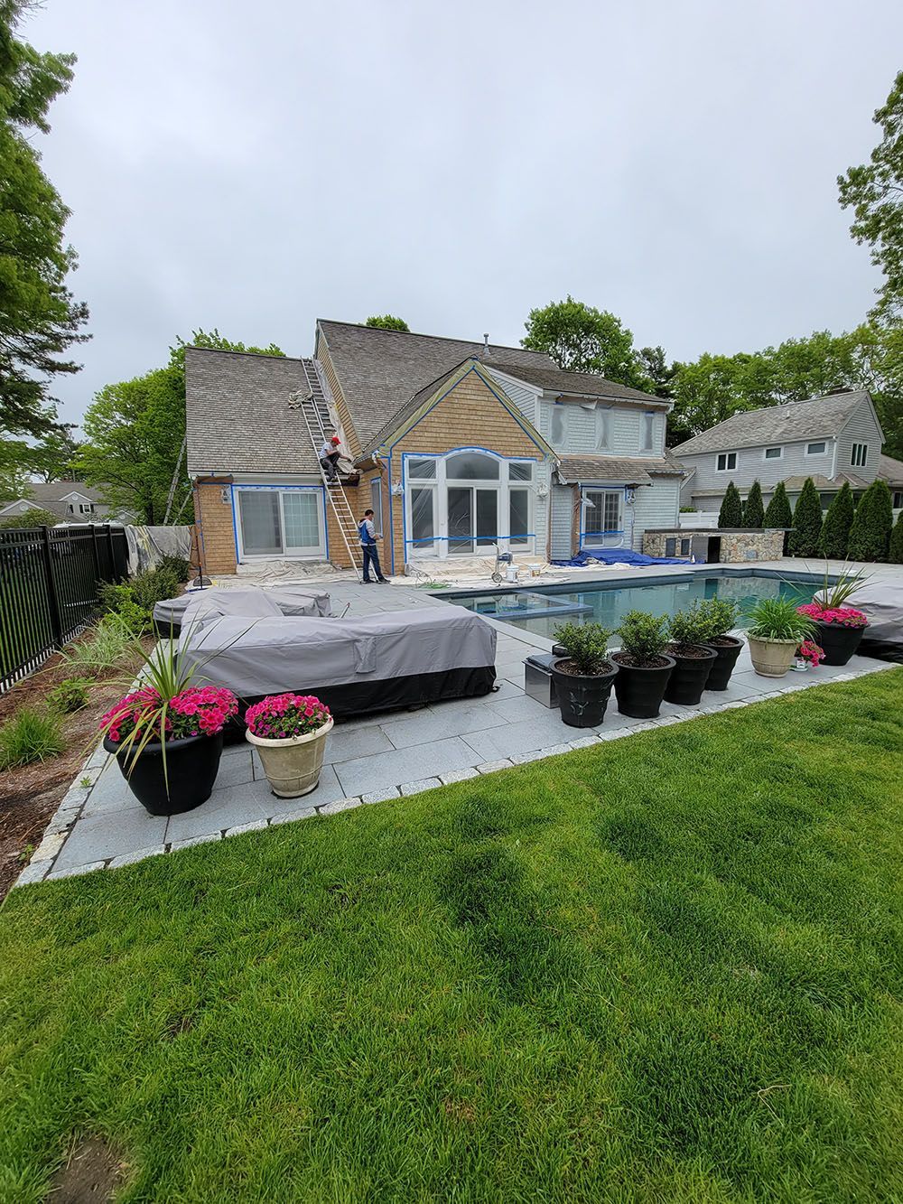 Stone house with patio, blue pool, potted flowers, and green lawn in a garden setting