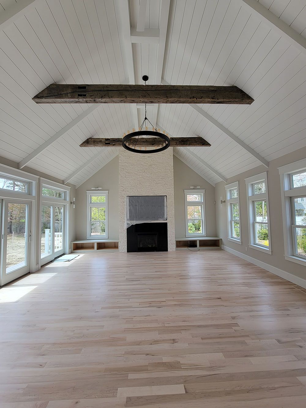 Bright sunroom with vaulted white ceiling, wood floors, fireplace, and large windows.