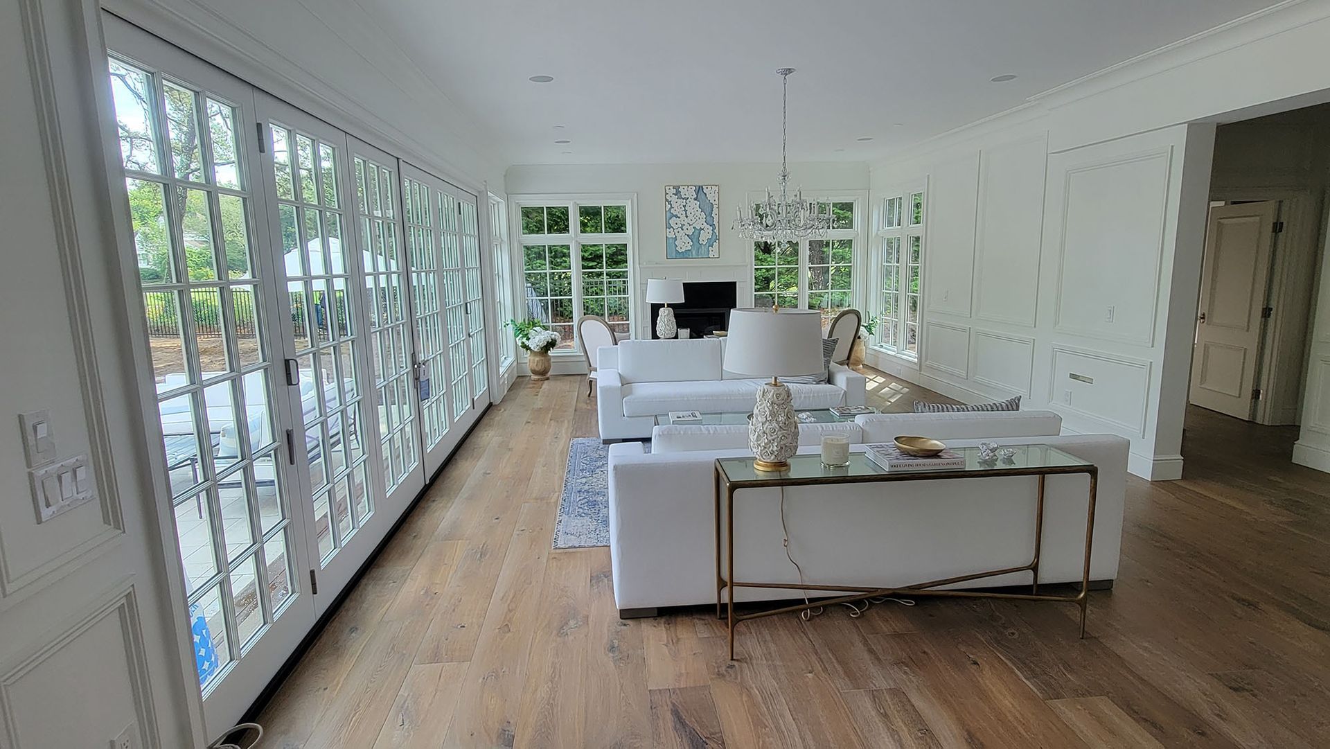 Bright, modern living room with white sofas, wood floors, and large windows overlooking greenery