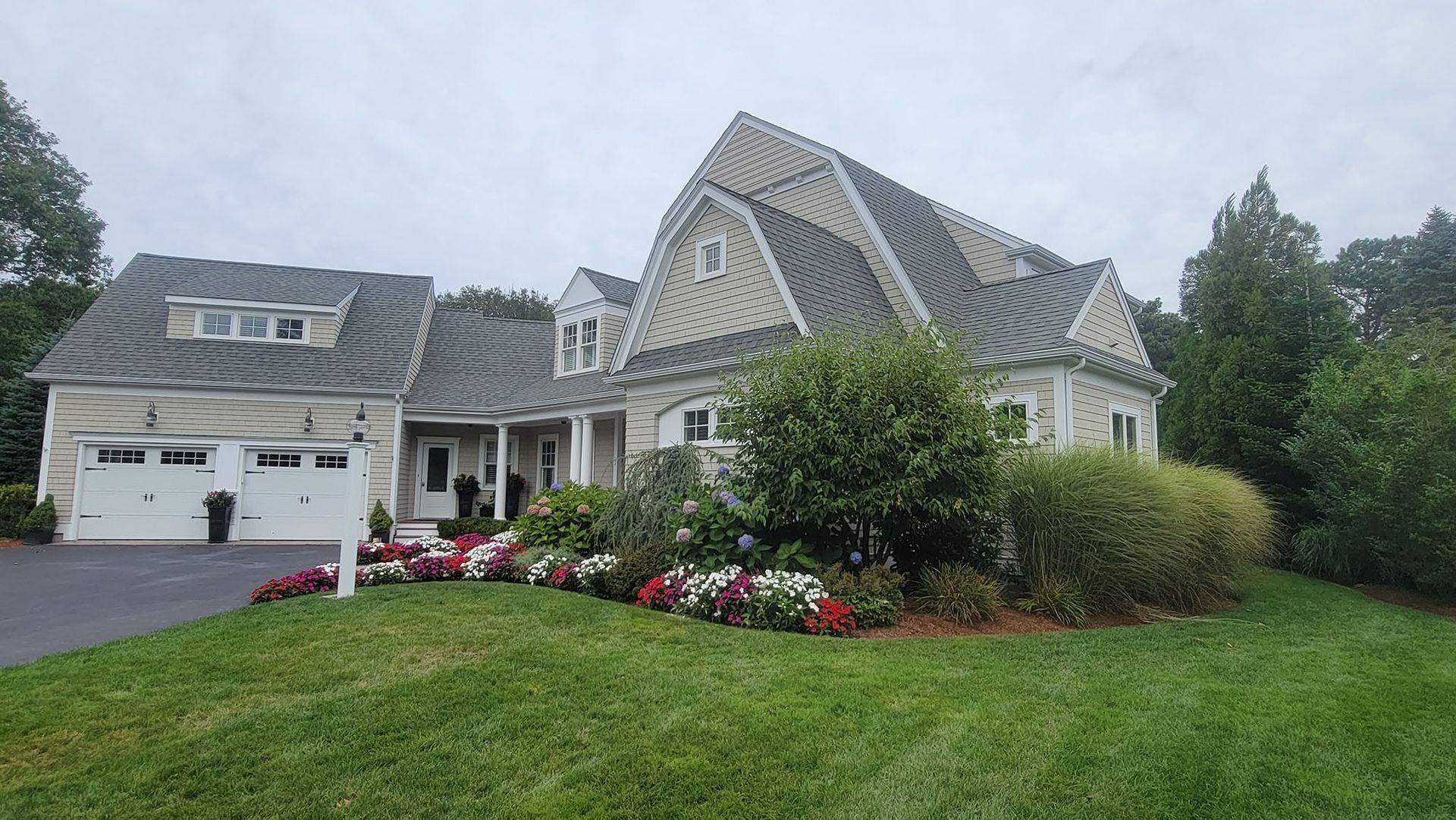 Large suburban house with stone exterior, two garages, and a flowerbed in front of a green lawn.