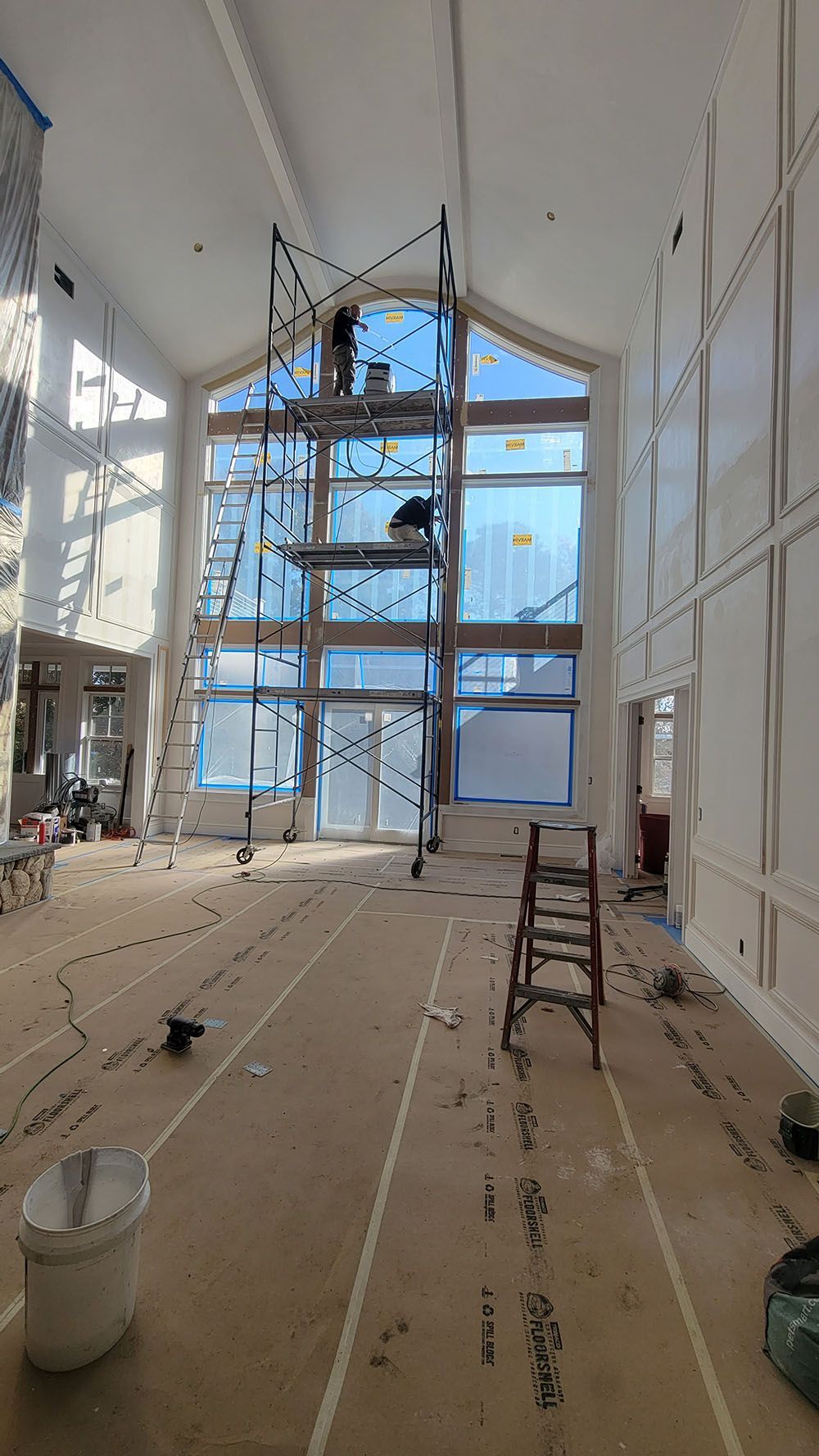 Tall unfinished room with scaffolding, ladder, and large blue-tinted windows under renovation