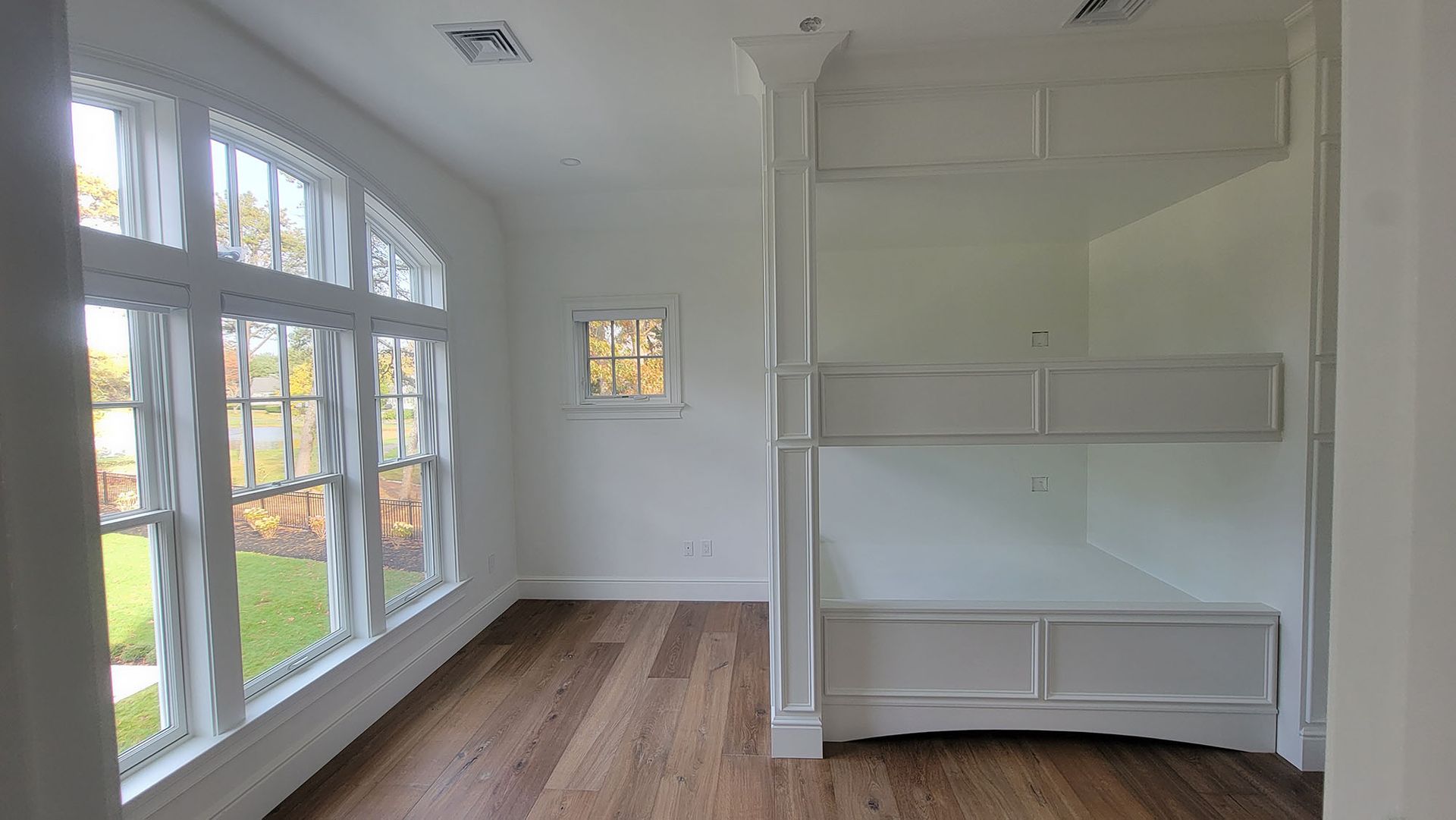 Bright white room with large arched windows, wood floors, and built-in shelving/bench seating