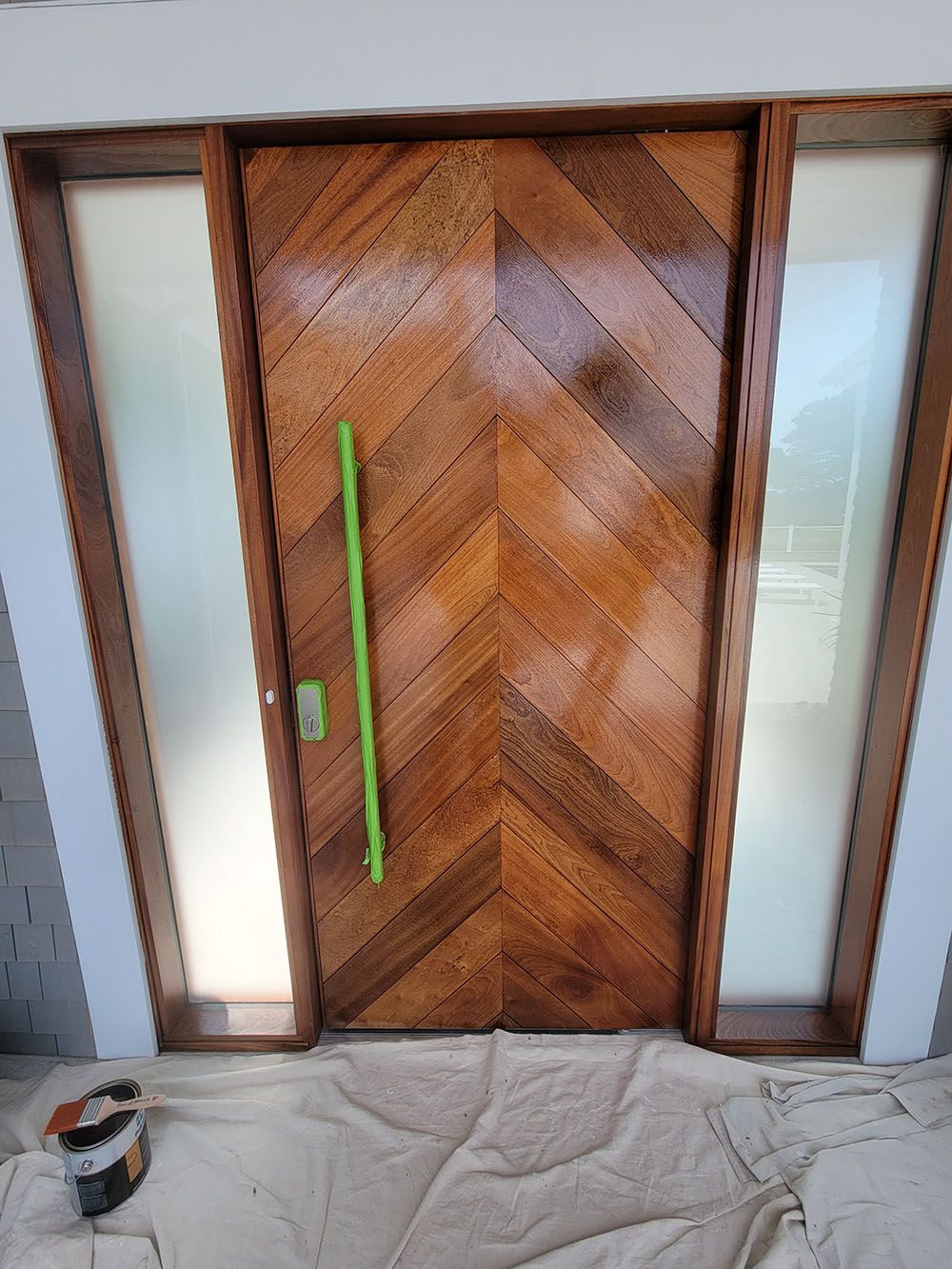 Wooden front door with chevron pattern, frosted glass side panels, and a green handle wrapped in tape
