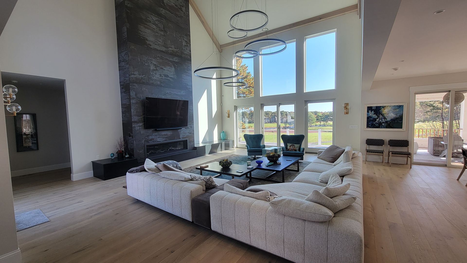 Modern living room with white sectional sofa, black fireplace, large windows, and hardwood floors