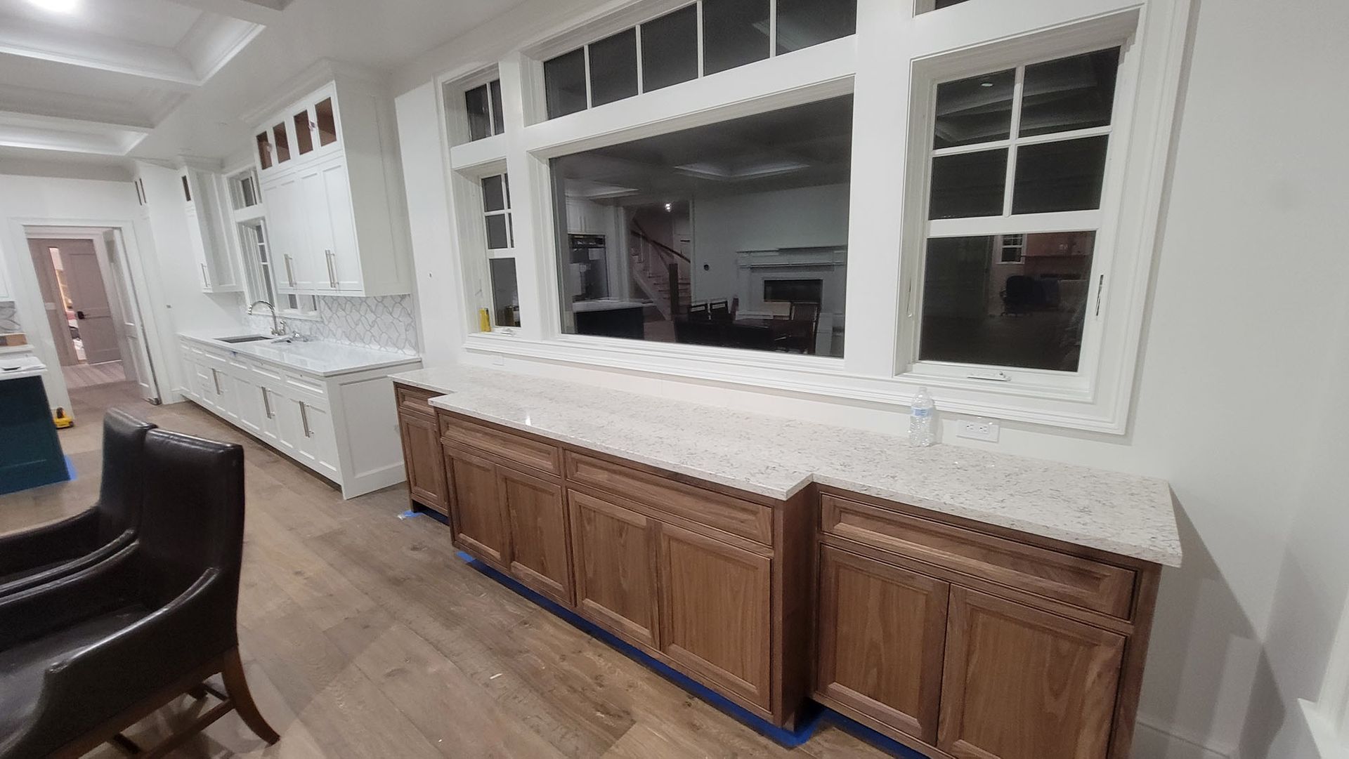 Bright kitchen with white cabinets, large windows, and wooden island cabinets along the wall