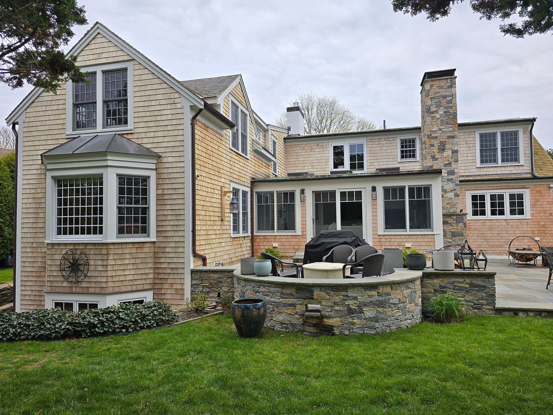 Stone house with bay windows, patio seating, and a green lawn in the backyard.