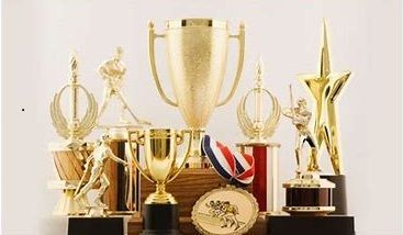 Golden trophies of various sizes and shapes, arranged on a white surface.
