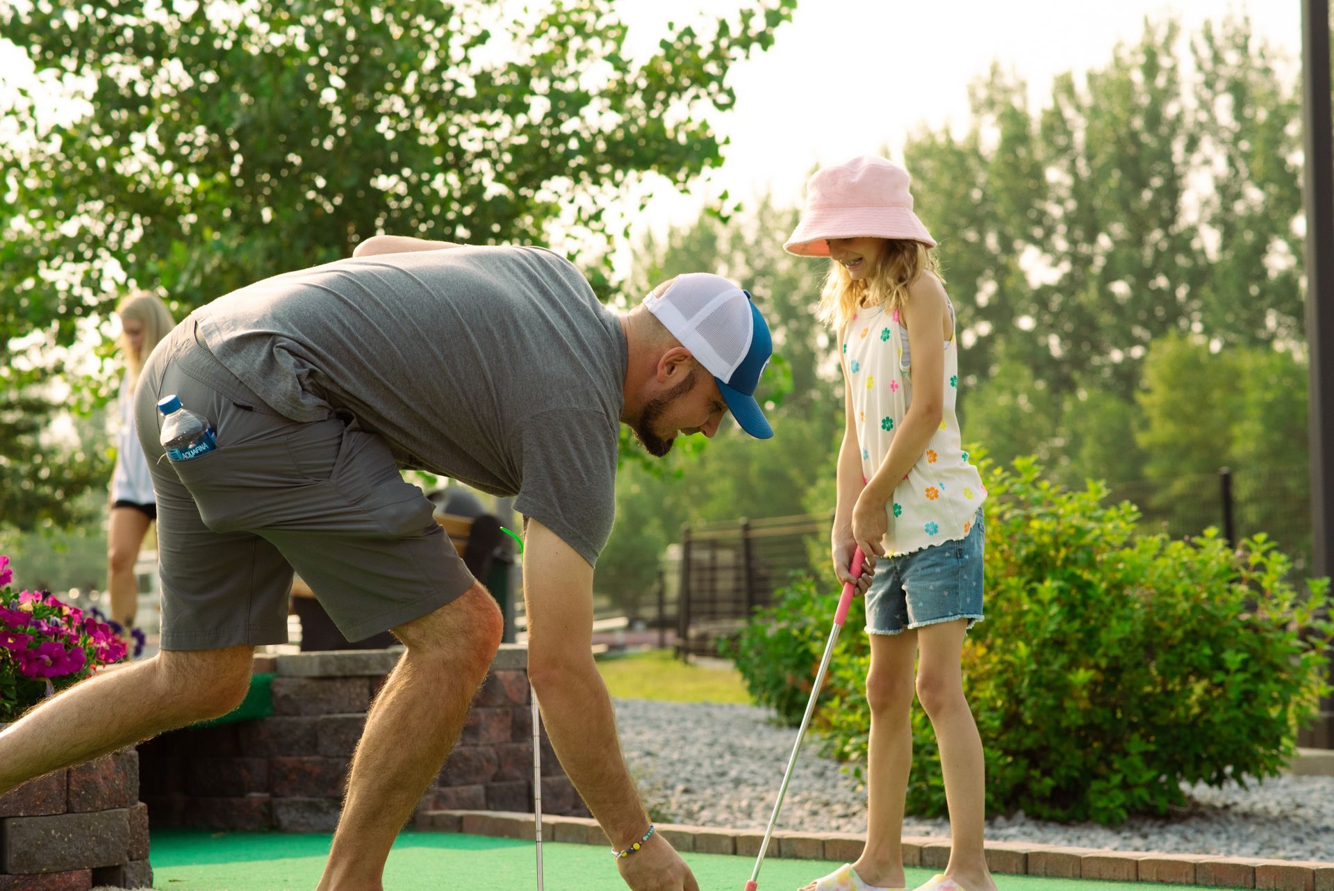 A man and a little girl are playing mini golf.