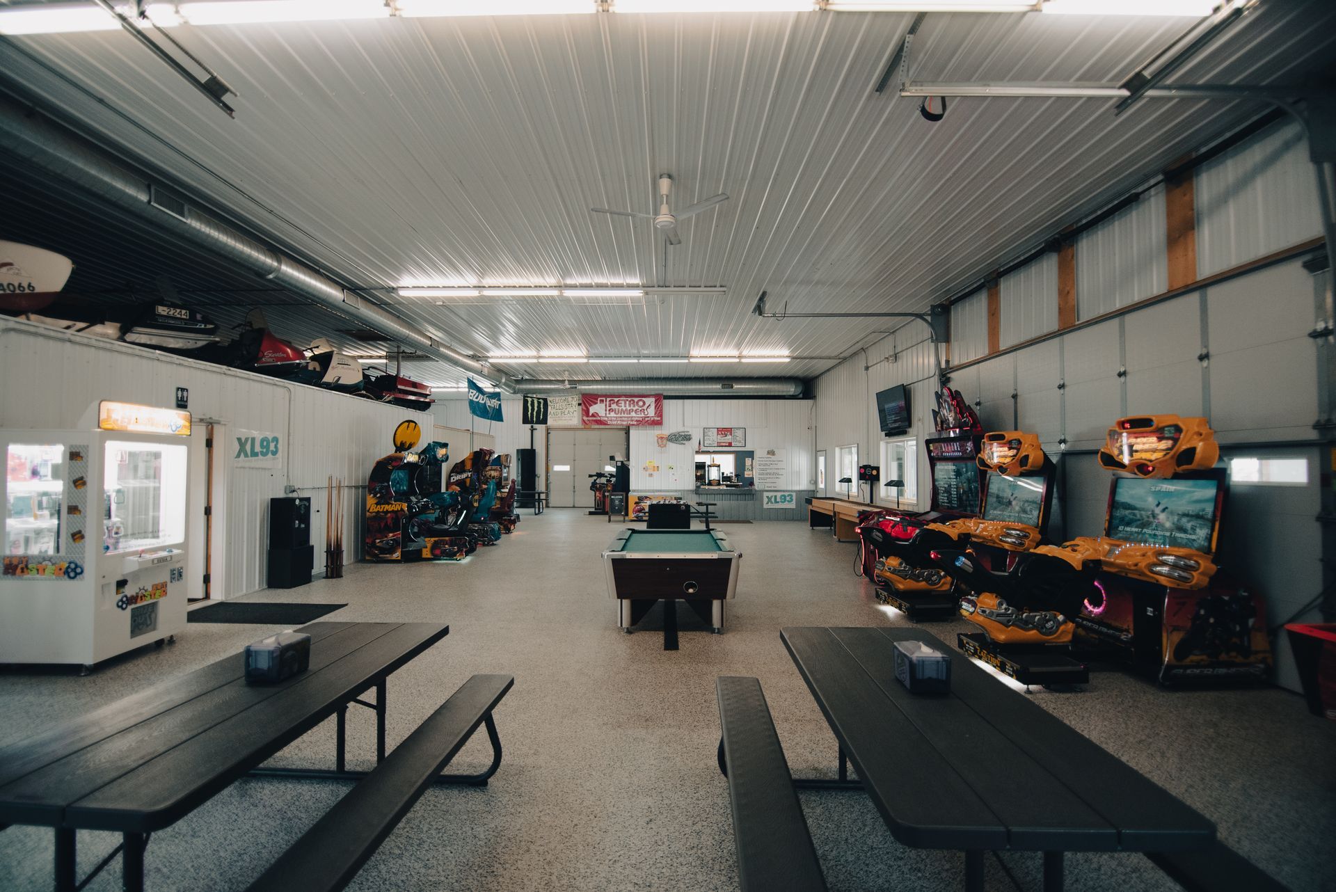 A large room with a pool table, picnic tables, and arcade games.