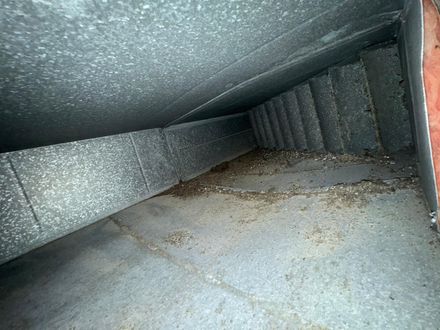 Interior of a galvanized metal air duct showing a section of interior insulation and debris on the bottom surface.
