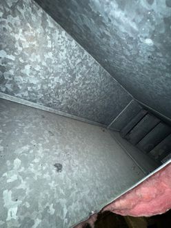 An interior view of a galvanized metal HVAC duct, showing smooth surfaces, seams, and exposed pink fiberglass insulation.