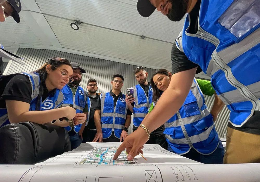People in blue safety vests review plans around a table in a meeting room.