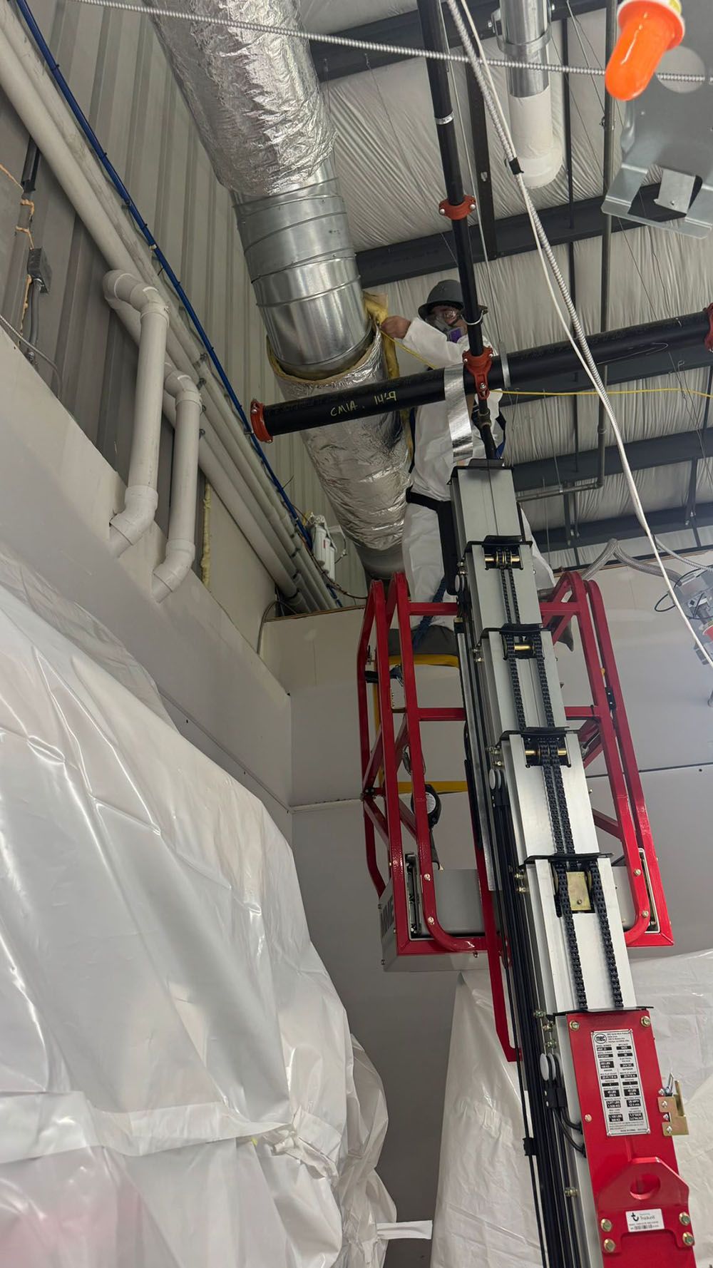 Red scissor lift in an industrial interior with exposed ducts and pipes near the ceiling