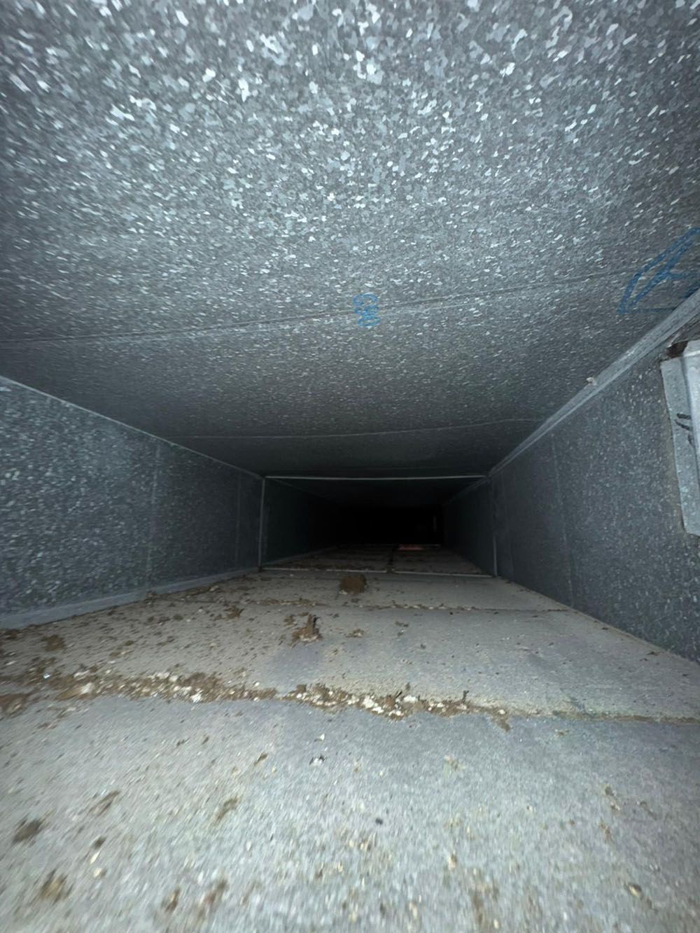 Inside a dusty metal ventilation duct with a dark opening at the far end