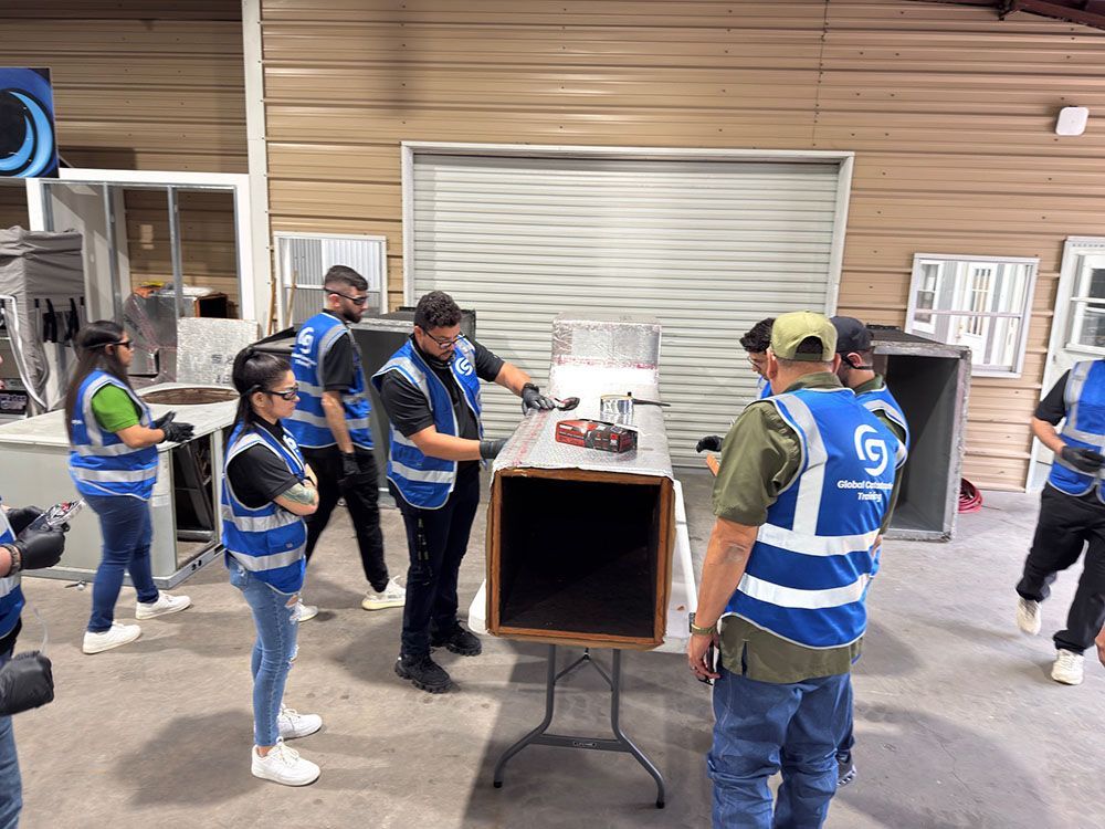 People in blue safety vests gather around a table and open crate in a warehouse-like room.
