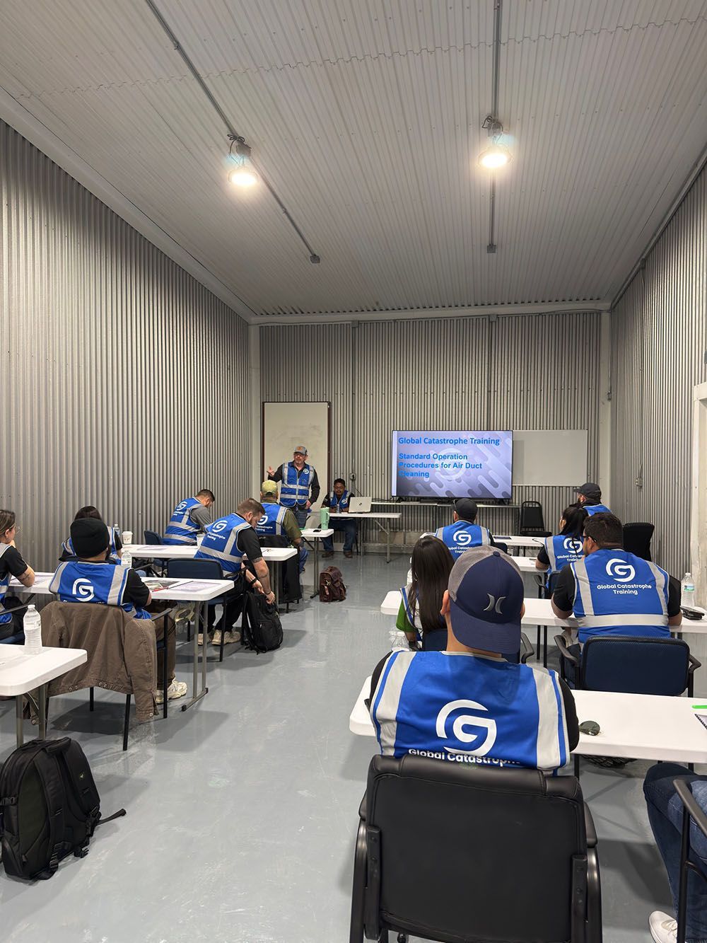 Classroom training session with people in blue shirts seated at desks facing a presentation screen
