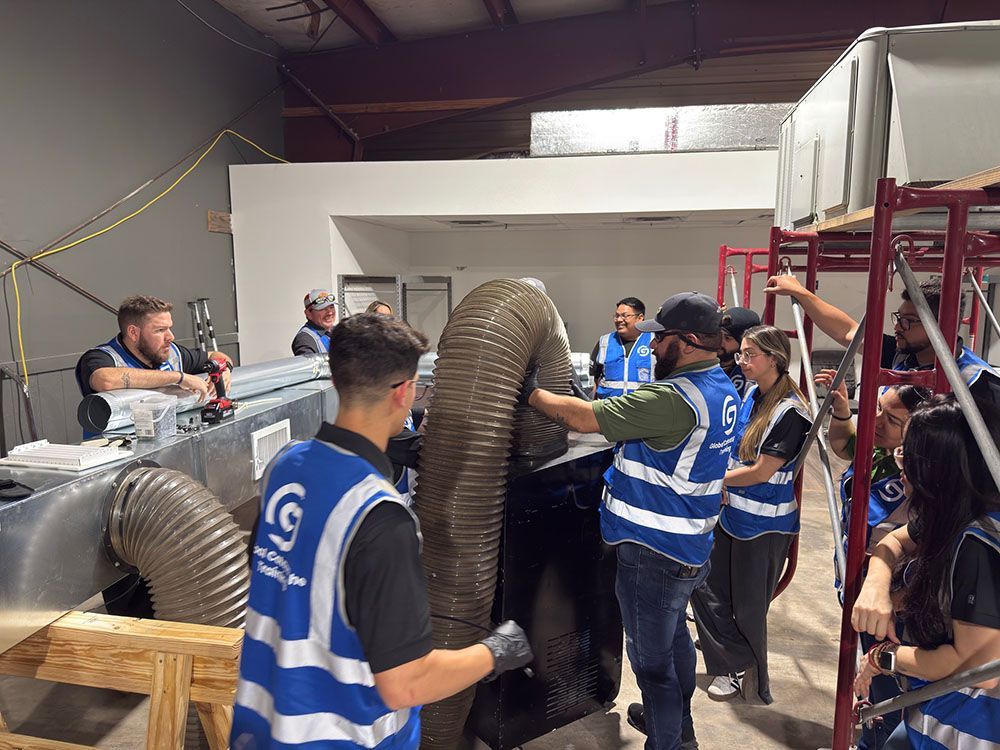 Workers in blue safety vests moving a large flexible duct inside an industrial workshop