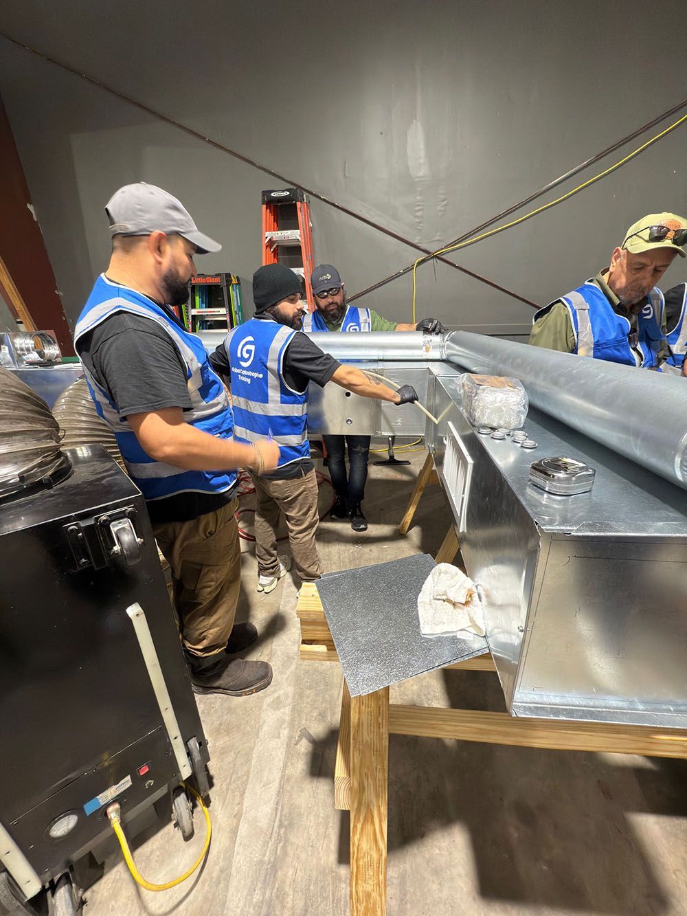 Workers in blue shirts assembling metal ductwork in an industrial shop