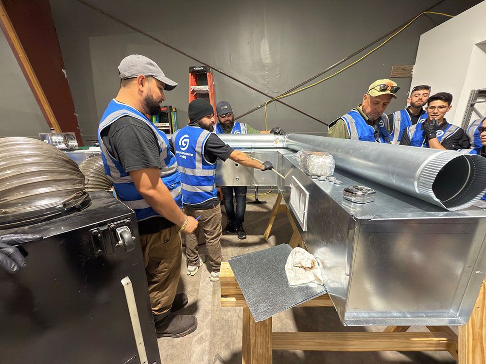 Workers inspect a large metal duct in a workshop, with tools and equipment nearby.