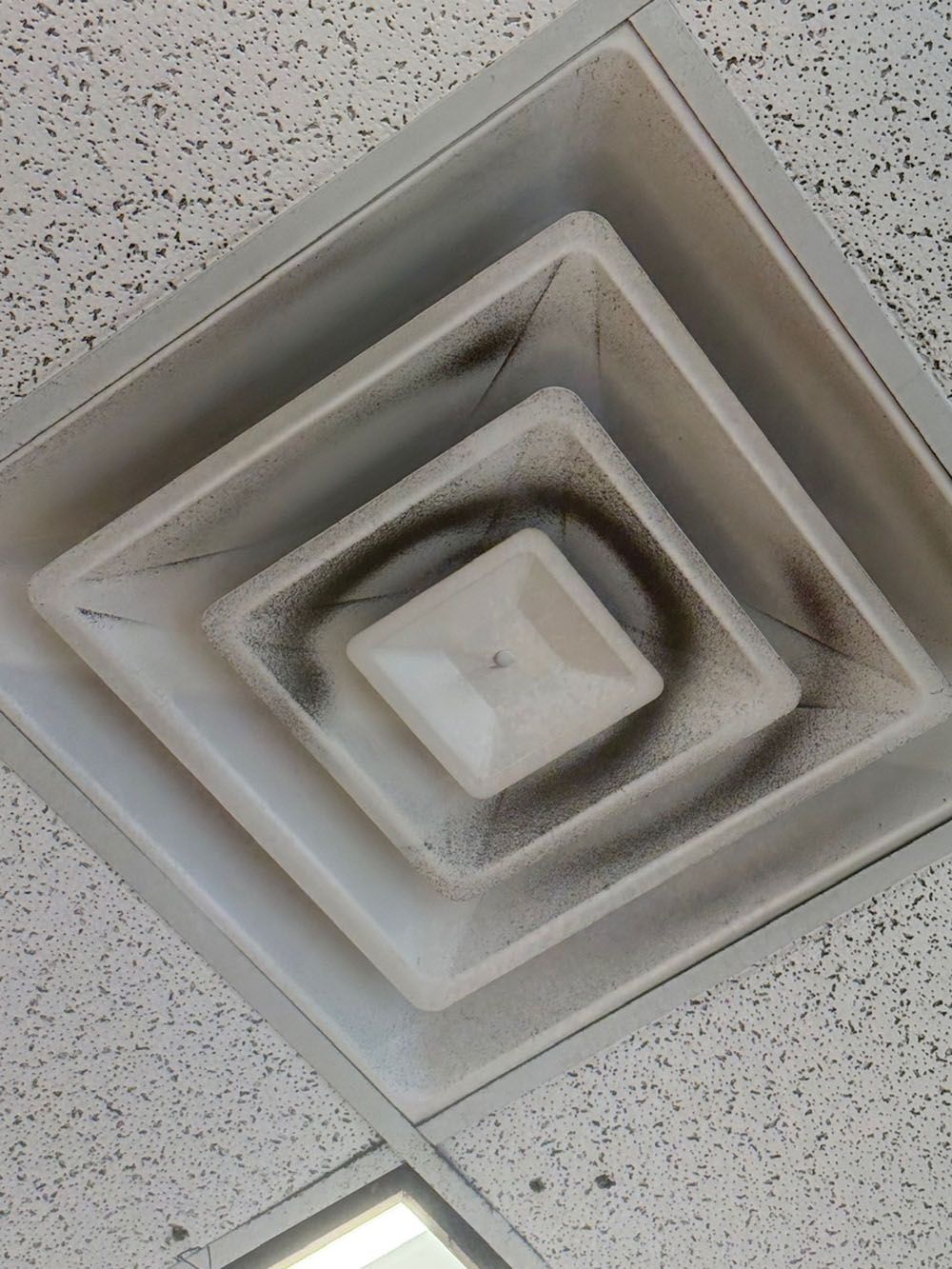 Ceiling air vent with concentric square grilles on a speckled tile ceiling