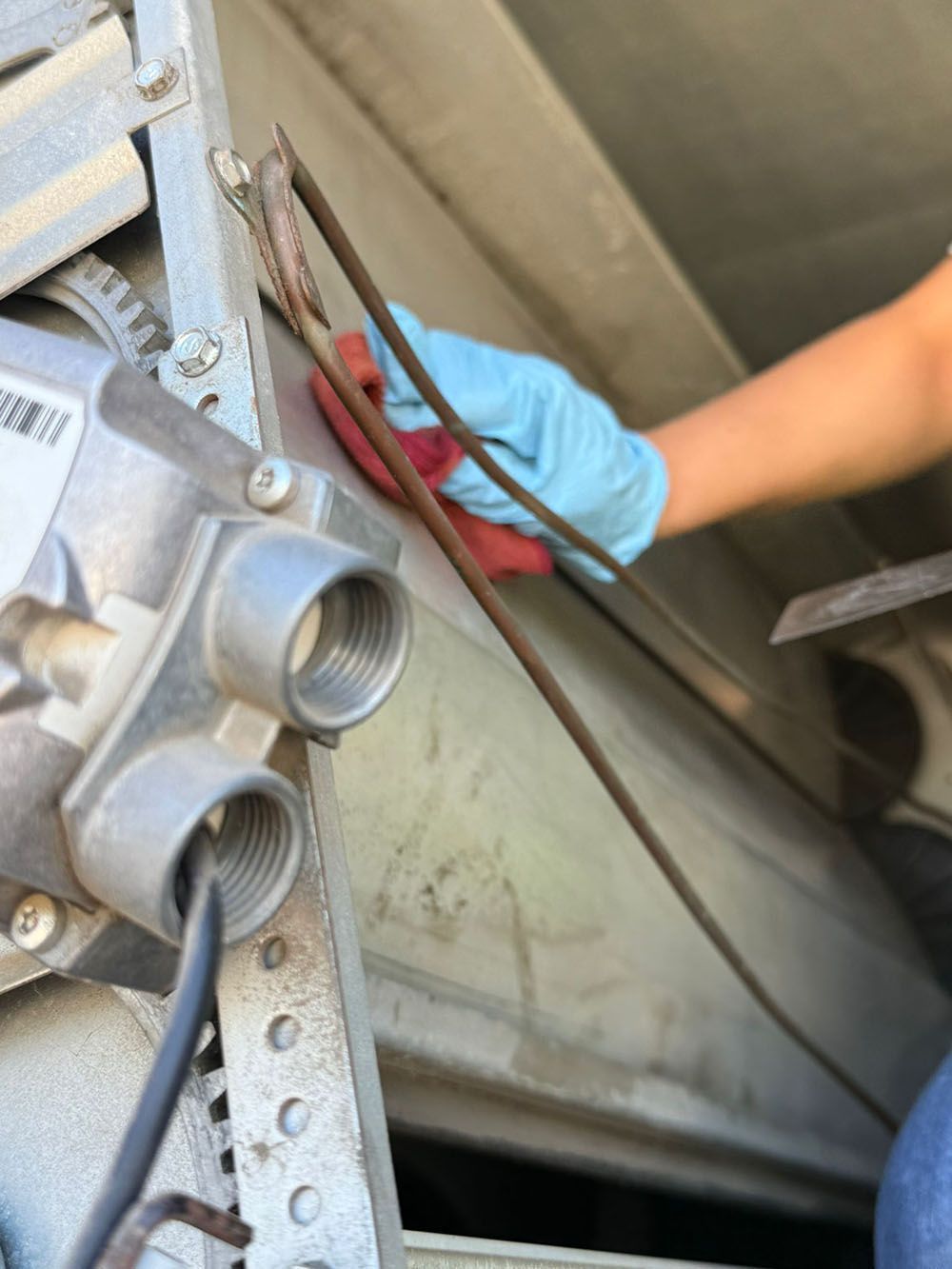 Blue-gloved hand working on metal machinery with red wires and threaded fittings