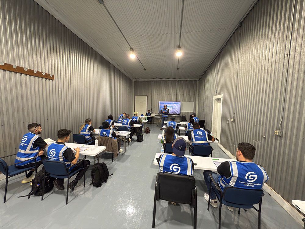 People in blue jerseys seated in a long meeting room, watching a presentation on a screen.