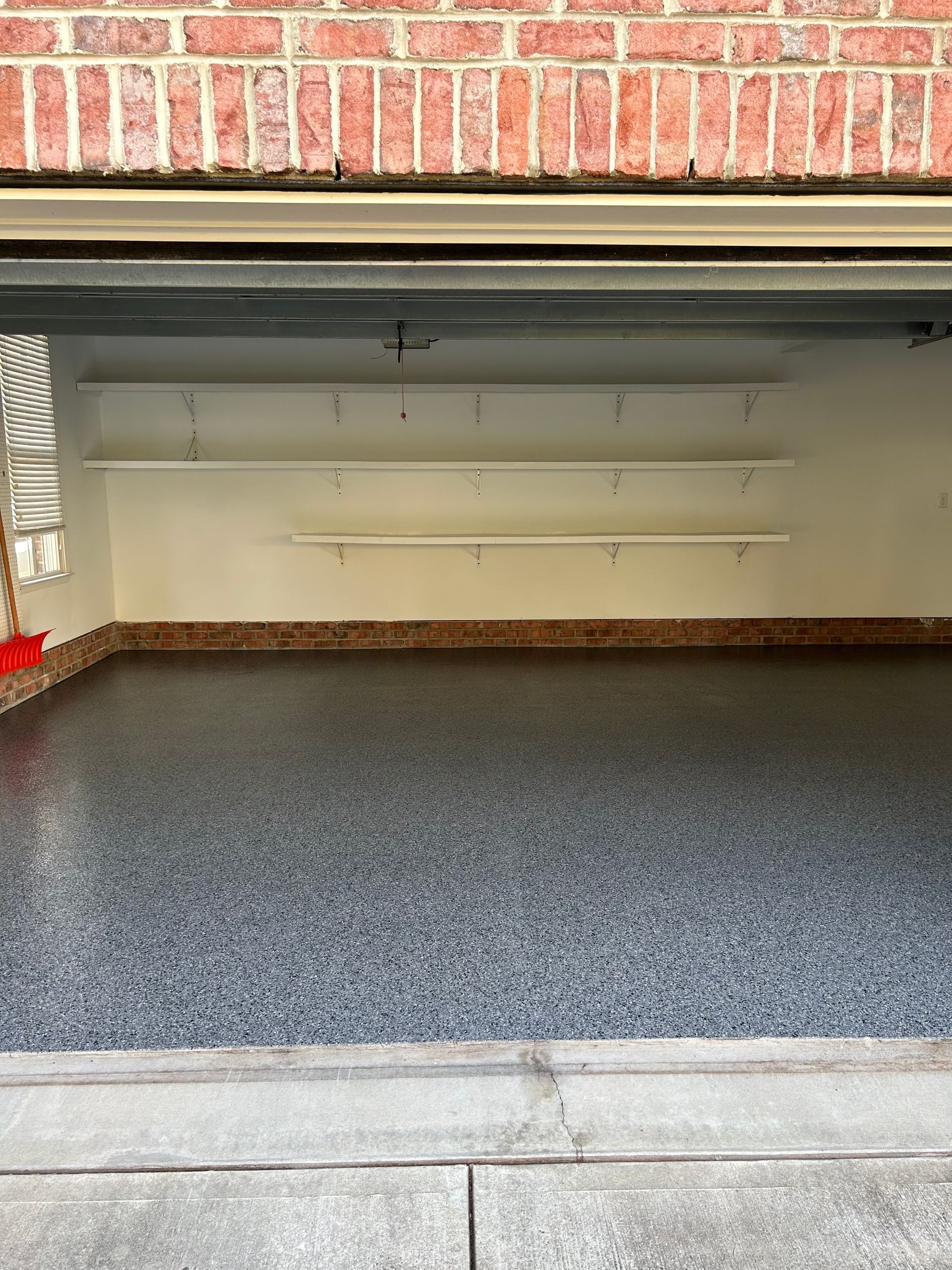 An empty garage with a brick wall and a gray floor.