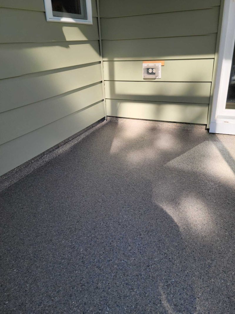 A patio with a concrete floor and a green siding on a house.