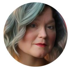 Close-up portrait of a person with wavy silver-blue hair and red lipstick on a white background