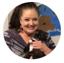 Smiling woman holding a black-and-white animal in front of a painted classroom mural