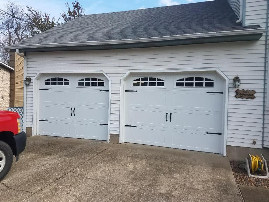 Two white double garage doors on a beige house with a concrete driveway and part of a red truck visible at left