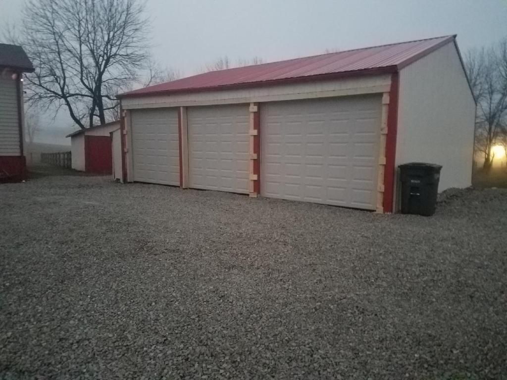 Three-car garage with beige doors, red roof, and gravel driveway at dusk
