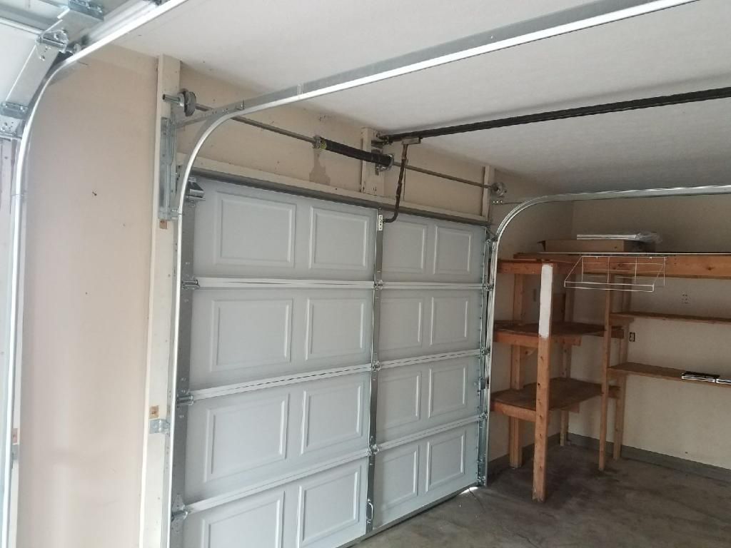 Open garage with white sectional door and shelving along the right wall.