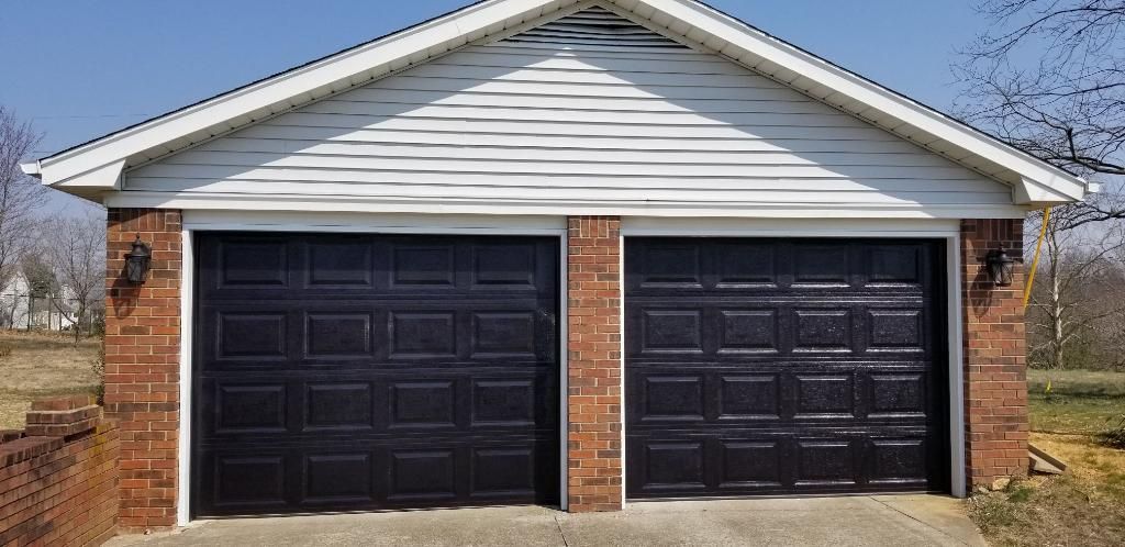 Two-car garage with black doors and white siding on a brick house