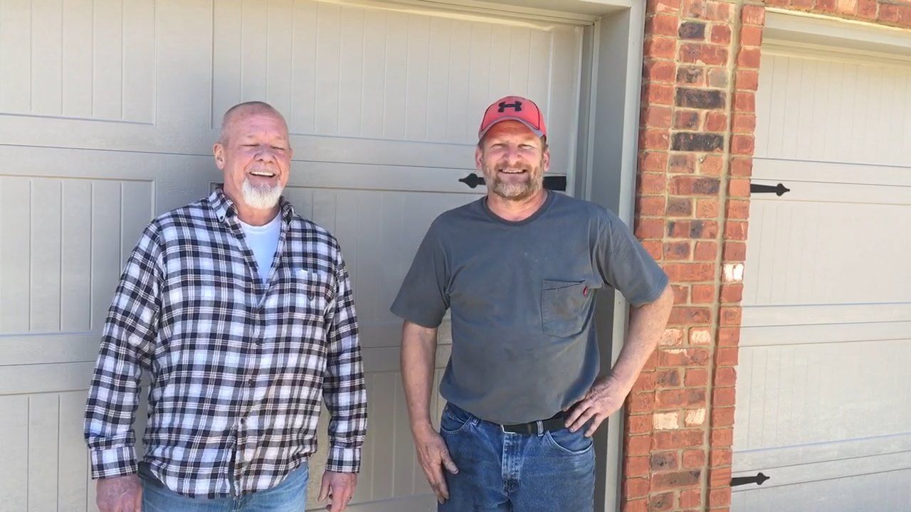 Two men standing and smiling in front of a garage and brick house exterior
