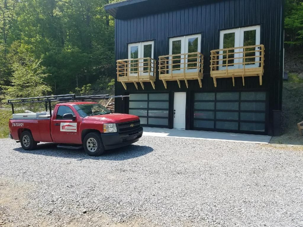 Red pickup truck parked beside a dark building with wooden balconies on a gravel lot