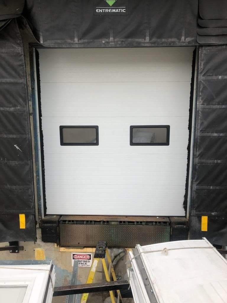Closed white loading dock door with two small windows, framed by black dock shelter curtains.