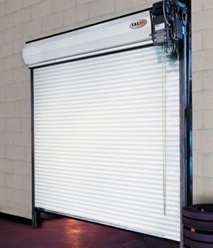 Closed white metal roll-up garage door inside a building, with a motorized opener on the right.