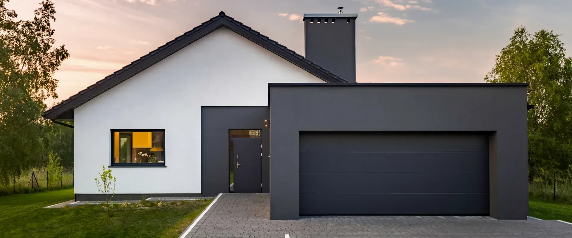 Modern white house with dark gray garage and roof at dusk