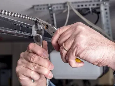 Hands using pliers to crimp a cable in an electronics panel