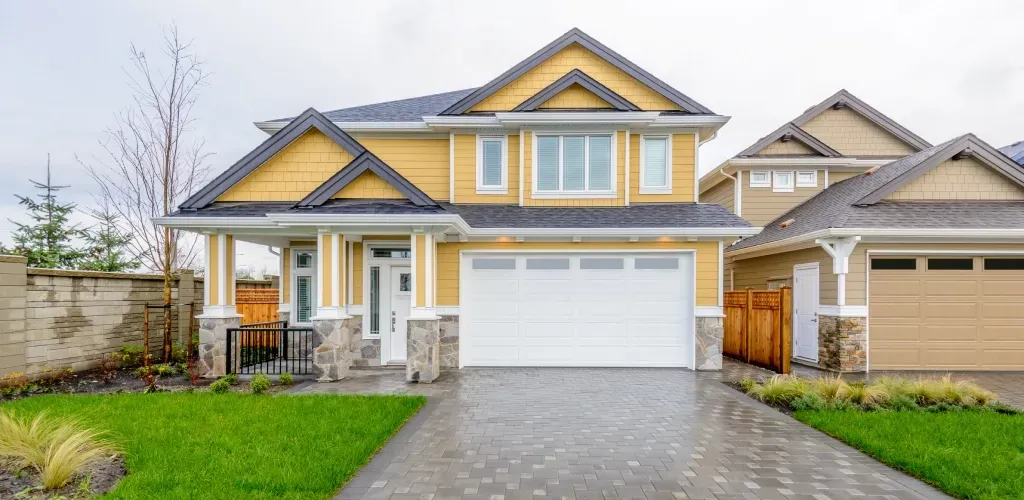 Suburban two-story house with white trim, gray garage door, and a paved driveway under cloudy skies