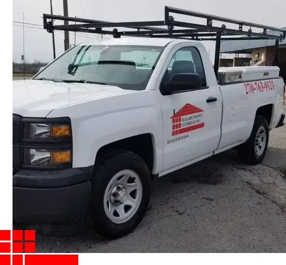 White pickup truck with a ladder rack parked on a street, viewed from the front-left side.