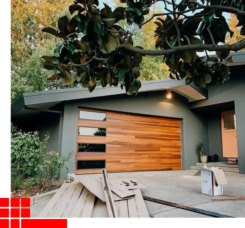 Modern gray house with wooden garage door, lit entry, and large tree branches overhead