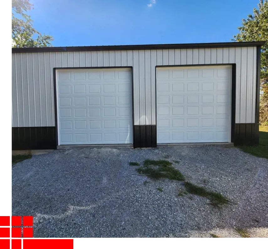 Two white garage doors on a metal-sided building with a gravel driveway and blue sky.
